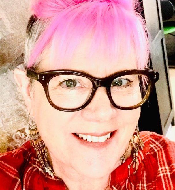 A smiling woman with pink hair wearing bold designer glasses in Durango.